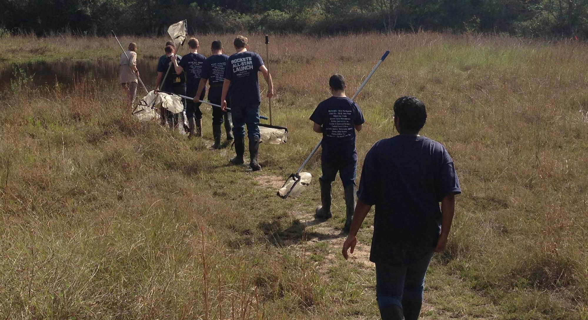 A field team carrying survey nets across a prairie